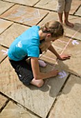 DESIGNER: CLARE MATTHEWS: GIRL DRAWING SNAKES AND LADDERS ON PATIO