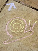 DESIGNER: CLARE MATTHEWS: SNAKES AND LADDERS. CHALK DRAWING OF SNAIL ON PATIO