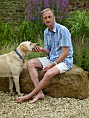 RICKYARD BARN GARDEN  NORTHAMPTONSHIRE: CLIVE SITTING ON A ROCK WITH MURPHY THE DOG