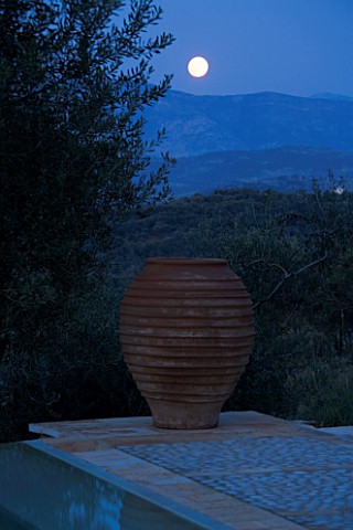 NIGHT_VIEW_ACROSS_SWIMMING_POOL_TOWARDS_TERRACOTTA_URN_WITH_FULL_MOON__IN_GINA_PRICES_CORFU_GARDEN