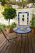 MEDITERRANEAN DECKED COURTYARD WITH STANDARD BAY  TILED WATER FEATURE AND MOSAIC TABLE. SHADE CANOPY. DECKING  TRELLIS  VINE  KATHY TAYLORS GARDEN  LONDON
