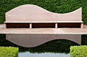 VEDDW HOUSE GARDEN  GWENT  WALES: DESIGNERS ANNE WAREHAM AND CHARLES HAWES - PINK SEAT/BENCH BESIDE REFLECTING POOL WITH A YEW HEDGE BEHIND