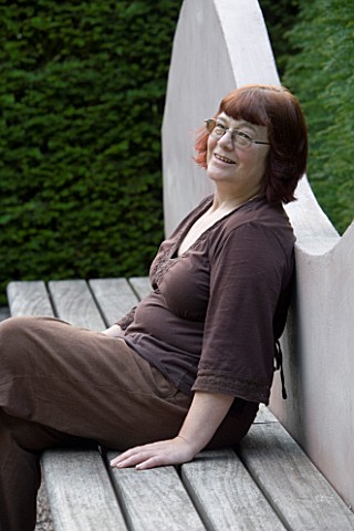VEDDW_HOUSE_GARDEN__GWENT__WALES_DESIGNER_ANNE_WAREHAM_SITS_ON_A_WAVE_BENCH_IN_THE_REFLECTING_POOL_G