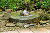 HUNMANBY GRANGE  YORKSHIRE: MILLSTONE WATER FEATURE SURROUNDED BY FERNS  GRAVEL AND ROCKS