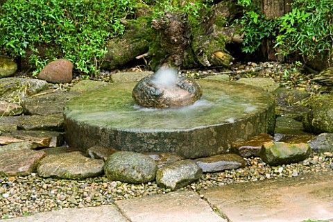 HUNMANBY_GRANGE__YORKSHIRE_MILLSTONE_WATER_FEATURE_SURROUNDED_BY_FERNS__GRAVEL_AND_ROCKS