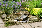 HUNMANBY GRANGE  YORKSHIRE: GRAVELLED AREA IN BORDER WITH CARVED STONE FEATURE WITH LEAF DESIGN & GARGOYLES. GERANIUM HIMALAYENSE GRAVETYE AND GOLDEN MARJORAM