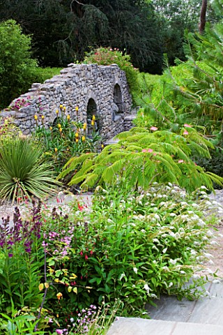 YEWBARROW_HOUSE_GARDENS__CUMBRIA__VIEW_DOWN_TO_THE_RUINED_WALL_WITH_MIMOSA_ALBIZIA_JULIBRISSIN_OR_PE
