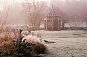 WOODPECKERS  WARWICKSHIRE  WINTER: FROSTY BORDER OF GRASSES  A STATUE AND EUPHORBIA WITH WOODEN SUMMERHOUSE BEHIND
