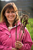 DESIGNER CLARE MATTHEWS - VEGETABLE PROJECT: CLARE HOLDING UP BARE ROOTED RASPBERRY MAILING JEWEL PLANTS READY FOR PLANTING