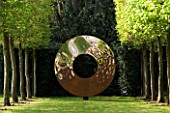DESIGNER: DAVID HARBER. GARDEN DESIGNED BY ANGEL COLLINS - RUSTY METAL CIRCLE SCULPTURE AT THE END OF A HORNBEAM AVENUE