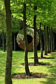 DESIGNER: DAVID HARBER. GARDEN DESIGNED BY ANGEL COLLINS - RUSTY METAL CIRCLE SCULPTURE AT THE END OF A HORNBEAM AVENUE.