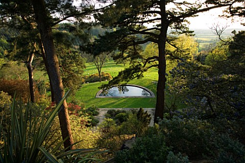 KIFTSGATE_COURT__GLOUCESTERSHIRE_THE_LOWER_GARDEN_AND_SWIMMING_POOL_SEEN_THROUGH_THE_SCOTCH_FIRS