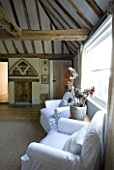 BOONSHILL FARM  EAST SUSSEX. INTERIOR OF BEDROOM WITH WOODEN FLOORBOARDS  EXPOSED BEAMS AND LINEN COVERED ARMCHAIRS AND MIRROR MADE FROM OLD WINDOW. DESIGNER: LISETTE PLEASANCE