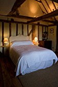 BOONSHILL FARM  EAST SUSSEX. INTERIOR OF BEDROOM WITH WOODEN FLOORBOARDS  EXPOSED BEAMS  FRENCH BEDHEAD AND OLD METAL SIDE TABLES. DESIGNER: LISETTE PLEASANCE