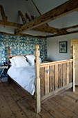 BOONSHILL FARM  E SUSSEX. INTERIOR OF BEDROOM WITH RECLAIMED WOODEN BED BY MICK SHAW FROM OLD STAIRCASE AND FLOORBOARDS. PEACOCK BLUE WALLPAPER DECORATES WALL. LISETTE PLEASANCE