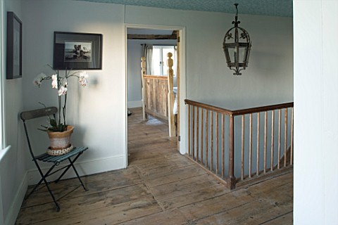 BOONSHILL_FARM__EAST_SUSSEX_INTERIOR_OF_LANDING_WITH_WOODEN_STAIRCASE__ANTIQUE_METAL_LANTERN__ORCHID