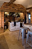 BOONSHILL FARM  E SUSSEX. INTERIOR OF KITCHEN WITH AGA  BRICK CANOPY WITH PANS & OLD BUTCHERS BLOCK. GALVANISED FRENCH STOOLS BY XAVIER PAUCHARD 1934 D: LISETTE PLEASANCE