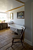 BOONSHILL FARM  EAST SUSSEX. INTERIOR OF BATHROOM WITH OLD ROLLTOP (CLAWFOOT) BATH & ANTIQUE CHAIR FROM INDONESIA. SHELVING MADE FROM TREE TRUNKS BY MICK SHAW. D: LISETTE PLEASANCE