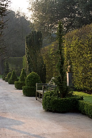HOLKER_HALL__CUMBRIA__THE_SUNKEN_GARDEN_AT_DUSK_WITH_BOX_HEDGING__WOODEN_BENCH__SEAT__AND_STATUARY_F