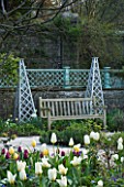 HOLKER HALL  CUMBRIA -THE SUNKEN GARDEN IN SPRING WITH TULIPS  WOODEN TRIPODS AND WOODEN BENCH