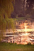 KELMARSH HALL  NORTHAMPTONSHIRE: VIEW AT SUNSET OF THE SUN SETTING ON THE LAKE OVERHUNG BY WEEPING WILLOWS