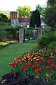 PASHLEY MANOR  EAST SUSSEX: TULIPS IN THE FOREGROUND WITH THE WALLED GARDEN AND MANOR HOUSE BEHIND