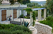 CORFU  GREECE: VILLA IN NORTH EAST CORFU. DESIGN BY ALITHEA JOHNS OF SKOPOS DESIGN AND RAHDY ELWAN. PATIO AT FRONT OF VILLA WITH PERGOLA  SEAT AND CONTAINERS