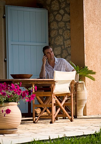 CORFU__GREECE_MAN_AGED_35_TALKING_ON_A_MOBILE_PHONE_AT_A_TABLE_PATIO__TABLE_AND_CHAIRS_RELAXED__BUSI