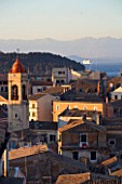 CORFU  GREECE: VIEW OF CORFU TOWN ROOFTOPS AT SUNSET WITH CORFU MOUNTAINS BEHIND