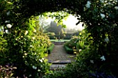 MARINERS GARDEN  BERKSHIRE. DESIGNER FENJA ANDERSON - VIEW INTO THE ROSE GARDEN THROUGH AN ARCH (MOON GATE) OF ROSE CITY OF YORK TO THE WATER LILY POOL WITH HERON SCULPTURE.