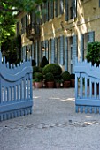 DESIGNER DOMINIQUE LAFOURCADE  PROVENCE  FRANCE -  ORNATE BLUE WOODEN GATE WITH FARMHOUSE BEHIND AND TERRACE WITH TERRACOTTA CONTAINERS AND BOX BALLS