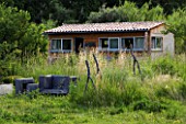 PROVENCE  FRANCE. GARDEN OF MARCO NUCERA. THE HOUSE WITH WOODEN BENCHES AND WOOD SCULPTURE IN LONG GRASS