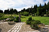 PROVENCE  FRANCE. GARDEN OF MARCO NUCERA. GRAVEL GARDEN WITH WOODEN SCULPTURE  STONE WATER TROUGH  WOODEN PATH AND TREES CLIPPED BY MARCO NUCERA