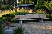 PROVENCE  FRANCE. GARDEN OF MARCO NUCERA. GRAVEL GARDEN IN MORNING LIGHT WITH LARGE WOODEN SEAT. A PLACE TO SIT