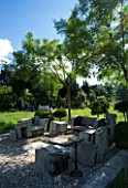 PROVENCE  FRANCE. GARDEN OF MARCO NUCERA. GRAVEL AREA WITH CHUNKY WOODEN FURNITURE