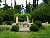 PROVENCE  FRANCE. GARDEN OF MARCO NUCERA. GRAVEL AREA WITH CLIPPED BALLS  STONE TABLE AND PILLARS PLANTED WITH A VINE
