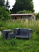 PROVENCE  FRANCE. GARDEN OF MARCO NUCERA. A PLACE TO SIT - CHUNKY WOODEN SEAT IN LONG GRASS WITH THE HOUSE BEHIND