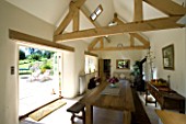 DESIGNER: CLARE MATTHEWS  DEVON: INTERIOR OF KITCHEN WITH WOOD BURNER  BESPOKE FARMHOUSE TABLE AND BENCHES  EXPOSED ROOF BEAMS AND LIMESTONE FLOOR. PATIO OUTSIDE