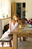 CLARE MATTHEWS HOUSE  DEVON. CLARE READING ON THE FARMHOUSE TABLE IN THE KITCHEN.