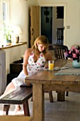 CLARE MATTHEWS HOUSE  DEVON. CLARE READING ON THE FARMHOUSE TABLE IN THE KITCHEN.
