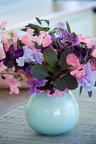 CLARE_MATTHEWS_HOUSE__DEVON_THE_KITCHEN_TABLE_WITH_BLUE_VASE_OF_SWEETPEAS