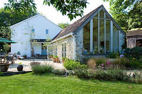 CLARE_MATTHEWS_HOUSE__DEVON_VIEW_FROM_GARDEN_TO_PATIO_AREA_AND_KITCHEN_EXTENSION_WITH_GLAZED_GABLE_E