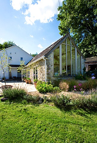 CLARE_MATTHEWS_HOUSE__DEVON_VIEW_FROM_GARDEN_TO_PATIO_AREA_AND_KITCHEN_EXTENSION_WITH_GLAZED_GABLE_E
