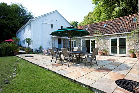 CLARE_MATTHEWS_HOUSE__DEVON_VIEW_FROM_GARDEN_TO_PATIO_AREA_WITH_TABLE_AND_CHAIRS_AND_KITCHEN_EXTENSI