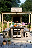 DESIGNER CLARE MATTHEWS: DEVON GARDEN. OUTDOOR SEATING AREA. PATIO WITH WOODEN TABLE AND BENCHES  COVERED PERGOLA AND OUTDOOR OVEN/ KITCHEN AREA