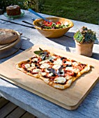 DESIGNER CLARE MATTHEWS: DEVON GARDEN. OUTDOOR SEATING AREA. WOODEN TABLE WITH PIZZA READY FOR COOKING