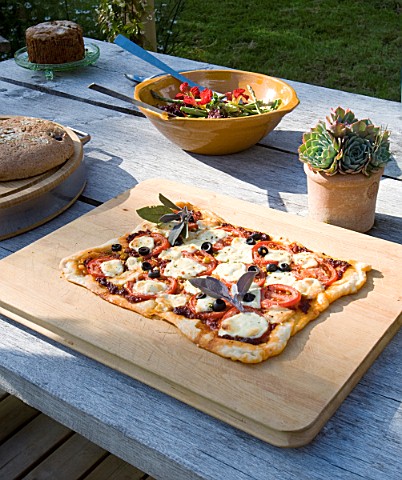 DESIGNER_CLARE_MATTHEWS_DEVON_GARDEN_OUTDOOR_SEATING_AREA_WOODEN_TABLE_WITH_PIZZA_READY_FOR_COOKING