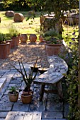 DESIGNER CLARE MATTHEWS: DEVON GARDEN. OUTDOOR SEATING AREA WITH CURVED WOODEN BENCH AND GRAVEL AREA WITH TERRACOTTA CONTAINERS