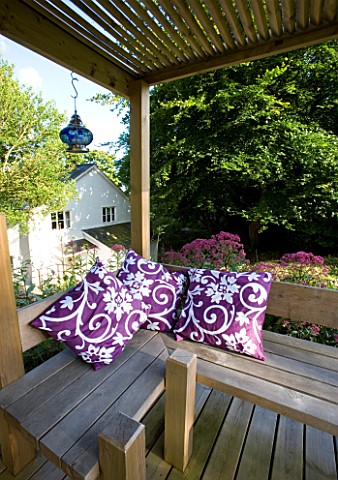 CLARE_MATTHEWS_GARDEN__DEVON_OUTDOOR_SEATING_AREA_WITH_WOODEN_PERGOLA_AND_BENCH_AND_PURPLE_CUSHIONS_