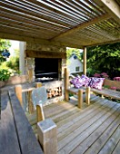 DESIGNER CLARE MATTHEWS: DEVON GARDEN. OUTDOOR KITCHEN WITH DECKING  OVEN AND BENCHES WITH PURPLE AND WHITE CUSHIONS